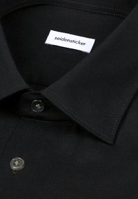 Chemise noire à col avec deux boutons noirs, montrant une étiquette de vêtement blanche imprimée avec le nom de la marque seidensticker.