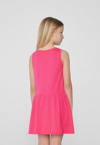 Robe sans manches fuchsia avec une jupe évasée, fabriquée en tissu doux. Elle présente un décolleté rond et est conçue pour un ajustement confortable.