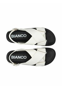 Witte crossband sandalen met zwarte zool, voorzien van metallic hardware accenten. Gelaagde banden met contrasterende kleuren en logo op de binnenzool.