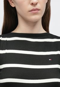 Must mustriline kampsun valgete horisontaalsete triipudega. Alumises vasakus nurgas on väike logo. Ümar kaelus. Puuduvad nähtavad kinnitused.