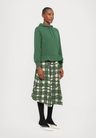 Felpa verde in cotone con coulisse e orlo a coste, abbinata a una gonna midi in plaid verde e crema, tights neri e scarpe con tacco bianche.