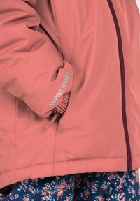 Rosa wasserdichte Jacke mit enganliegendem Ärmel, Reißverschluss und Markenaufdruck am Bündchen. Blumendesignstoff darunter sichtbar.