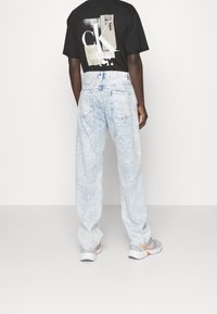 Jeans azul claro con efecto desgastado, de cintura alta y corte holgado, combinados con una camiseta negra con un estampado gráfico. Zapatillas blancas completan el look.