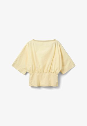 Blouse ample jaune clair avec manches larges, encolure bateau et détail de taille froncée sur fond blanc.