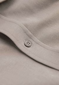 Gros plan sur un tissu beige avec des coutures visibles et un petit bouton à quatre trous cousu sur la couture.