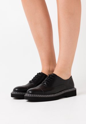 Černé kožené šněrovací boty se zaoblenou špičkou, hladkým povrchem, kontrastním bílým šitím a silnou platformovou podrážkou.