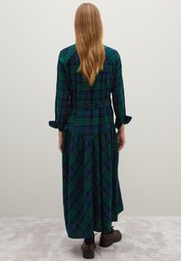 Vestido largo de cuadros en tonos verdes y azul marino, con botones delanteros, mangas largas y diseño de falda en capas con cintura ceñida con cinturón.