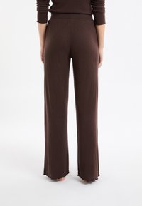 Braune, gerippte Strickhose mit weiter geschnittener Form und geschweiftem Saum. Verfügt über einen hohen Bund für Komfort. Ansicht von hinten.