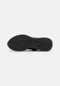 Suela de zapatilla negra con goma plana y texturizada, que presenta patrones en zigzag y espiga para ofrecer agarre y durabilidad. Diseño minimalista sin logotipo visible.