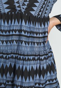 Robe noire et bleue à motifs géométriques. Le tissu est lisse avec une taille élastique et un détail de jupe froncée.
