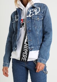 Giubbotto di jeans con dettagli sbiaditi, caratterizzato dalla scritta bianca "DEAD" sul davanti. Abbinato a una felpa bianca con cappuccio e jeans blu. Accenti in metallo argentato.