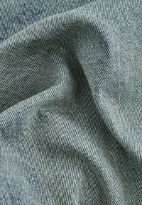 Tissu en denim de teinte bleu clair, présentant un motif de tissage en sergé. La texture semble douce avec des variations de couleur subtiles.