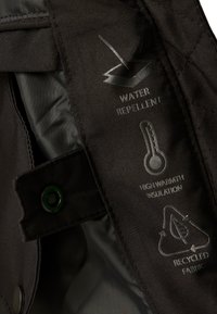 Close-up van de zwarte jacketstof met waterafstotend, hoge warmte-isolatie, en iconen en labels voor gerecycled stof.