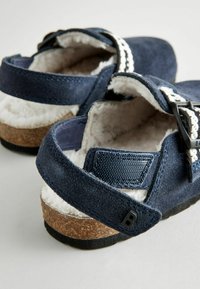 Marinblå sandaler med överdel av mocka, foder av päls, korksula och justerbara remmar. Har vit sömnad och en liten svart logodetalj.