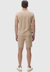 Beige polo shirt and shorts, made from soft material, with a relaxed fit. The outfit is completed with white sneakers featuring green accents.