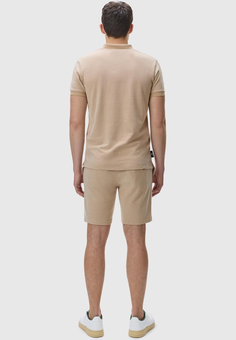 Beige polo shirt and shorts, made from soft material, with a relaxed fit. The outfit is completed with white sneakers featuring green accents.