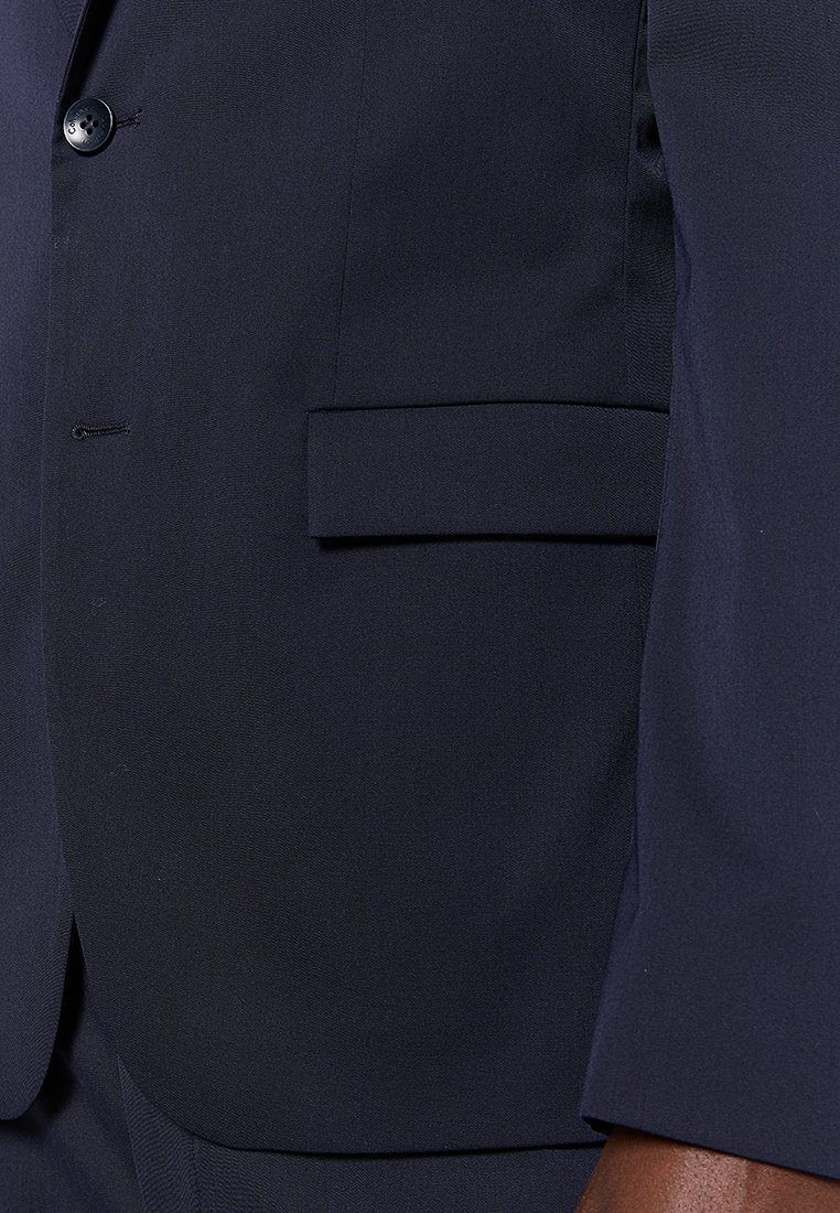 Blazer marine avec une texture lisse, fermeture à un seul bouton et une poche plate sur le côté gauche près de la taille. Coupe ajustée.