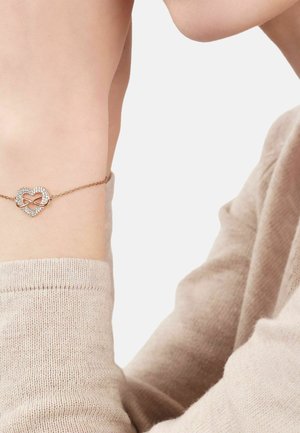 Muñeca con delicada pulsera de oro rosa que presenta un colgante en forma de corazón con un símbolo de infinito incrustado con pequeños cristales.