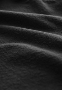 Tissu noir texturé avec des plis doux et ondulés, présentant une surface lisse et mate. L'éclairage met en valeur de subtiles variations de ton.