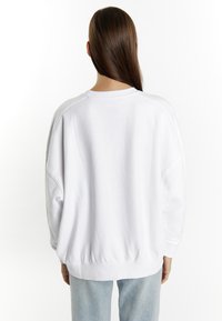 Witte oversized trui met een ronde hals, geribbelde boorden en tailleband. Zacht stof, casual pasvorm en verlaagde schoudernaht.