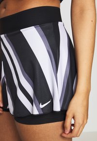 Skort en blanco y negro con rayas onduladas, hecho de tejido texturizado, que presenta una cinturilla ancha y un pequeño logo de Nike en la parte inferior.