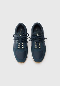 Marine sportieve schoenen met een bovenwerk van stof en leer, witte veters, beige accenten, rubberen zool en een zwart logo op de zijkant.