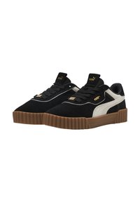 Zapatillas negras de ante con suelas de goma texturizada color ámbar, rayas laterales blancas y cordones negros. Presenta un logo dorado en la lengüeta.