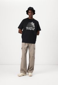 Svart t-skjorte med hvit "new balance running club" grafikk, parret med beige cargo-bukser og kremfargede sneakers, fullført med en svart bøttehatt.