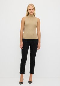 Top sans maniche color beige a coste con collo alto, abbinato a jeans neri aderenti e tacchi a punta. Design semplice con dettagli minimi.