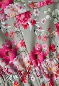 Blommigt tyg i nyanser av rosa på en grå bakgrund. Innehåller stora blommor, små blommor och gröna blad. Samlad texturdetalj synlig.