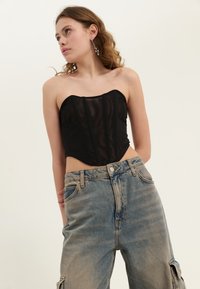 Svart mesh korsett topp med faste sømmer, kombinert med høyt liv og løstsittende blå denim jeans. Strukturert stoff med en uformell stil.