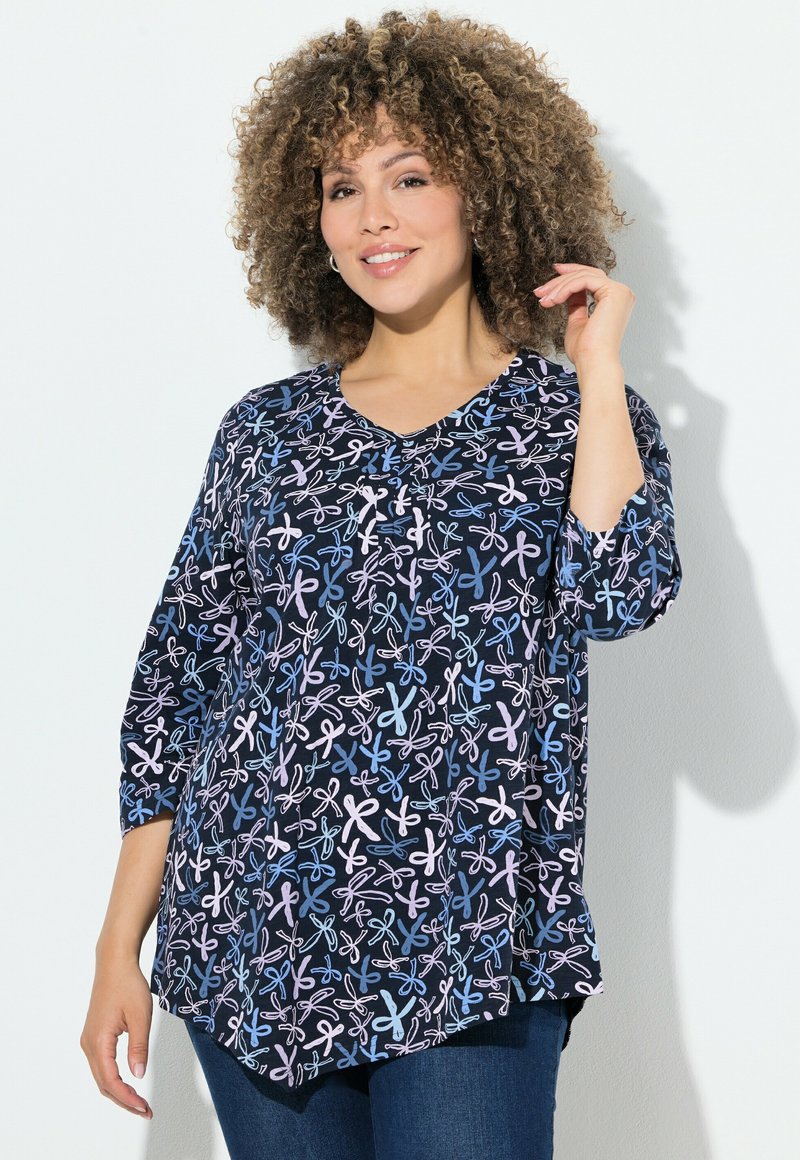 Donkerblauw top met een V-hals, met een speels patroon van roze en lichtblauwe lussen. Driekwart mouwen en een gebogen zoomontwerp.