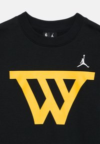 Camiseta de algodón negra con un gran gráfico amarillo de una "W" en el frente y un pequeño logo blanco de Jumpman encima. Diseño clásico con cuello redondo.