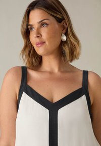 Blusa bianca con un contorno a V nero, dotata di spalline sottili e una texture liscia. Il colletto è ampio, creando un effetto stratificato.