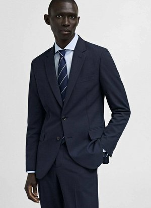 Navy suit with a structured blazer, single button closure, and notch lapels. Paired with a light blue shirt and dark striped tie.