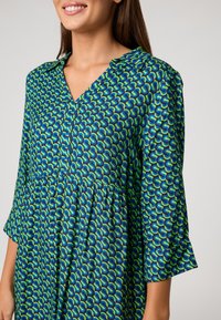 Blaue und grüne gemusterte Kleid mit V-Ausschnitt, Knopfdetails und 3/4-Ärmeln. Weicher Stoff mit gerafftem Taillenbund und ausgestelltem Rock.