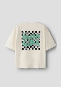 Camiseta oversize color crema con un gráfico colorido que incluye el texto "DREAM GIRL", flores y un fondo de cuadros en blanco y negro.