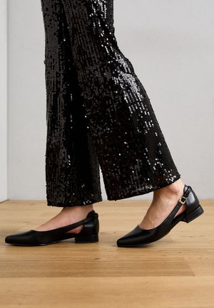 Sorte slingback flade sko med spids tå, mat lædermateriale og lille blokhæl, parret med glitrende sorte flagrende bukser.