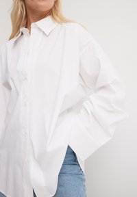 Balta liela krekliņa izgatavots no viegla auduma, ar norādītu apkakli, poga priekšā un platām piedurknēm. Apvienots ar gaiši ziliem džinsiem.