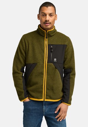 Grøn fleecejakke med sorte paneler, gule detaljer, fuld lynlås, høj krave og frontlynlås lomme. Har et tekstureret, hyggeligt stof.
