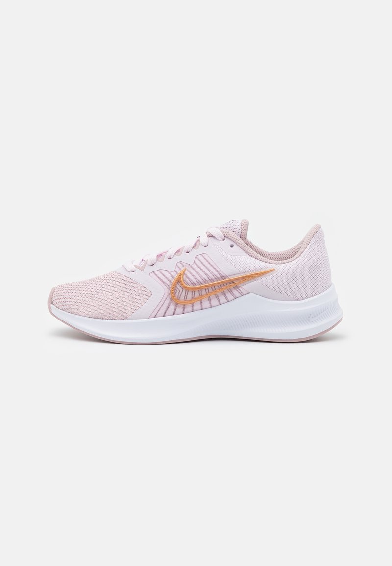 Chaussure de course athlétique rose clair avec semelle blanche et logo Nike swoosh orange sur le côté, vue de l'extérieur.