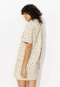 Robe beige à manches courtes avec un imprimé floral noir. Caractérisée par une coupe ample et un ourlet incurvé, elle est fabriquée en tissu léger.