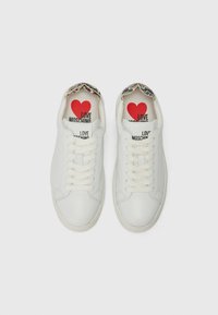 Balti odiniai sportbačiai su apvaliu nosiu, plokščiomis raišteliais ir raštuota apykakle. Vidus turi raudonai juodą grafikos spaudą.