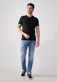 Juoda trumpomis rankovėmis V formos kaklo marškinėliai, derinami su šviesiai mėlynomis džinsomis ir juodais sportbačiais, pasižymintys aptakiu siluetu ir lygiu audinio paviršiumi.