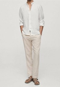Chemise en lin blanc avec un col montant, manches longues. Pantalon en lin beige clair. Sandales marron avec un design à lanières. Style minimaliste.