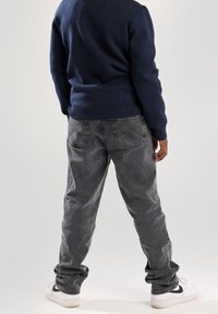 Pull bleu marine, poignets ajustés, et jean gris clair avec une coupe décontractée et une texture délavée. Des baskets blanches avec des accents noirs complètent le look.