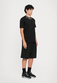 Svart t-skjorte med korte ermer, med hvit tekst på kragen. Kombinert med svarte løse shortser og svarte sneakers. Minimalistisk design.