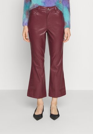 Vrouw draagt een high-waist, bordeauxrode leren cropped flare broek met steekzakken aan de voorkant, gecombineerd met zwarte pumps met puntige neus en een pluizige, meerkleurige trui.