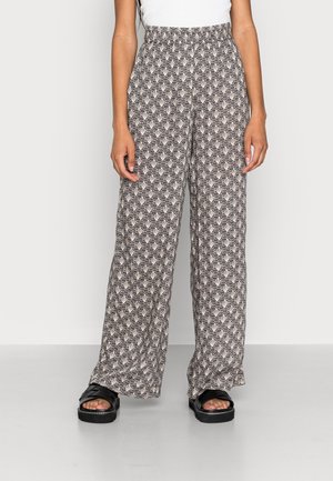 Mustavalkoinen geometrinen kuviointi leveälahkeisissa housuissa, yhdistetty mustiin korokepohjaisiin sandaaleihin ja valkoiseen hihattomaan toppiin.