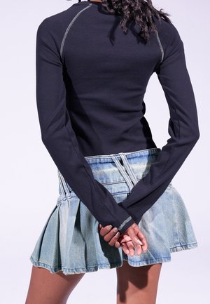 Sort top med lange ærmer kombineret med et lyseblåt plisseret denimskørt. Det har kontrastsyninger og et højtaljet design.